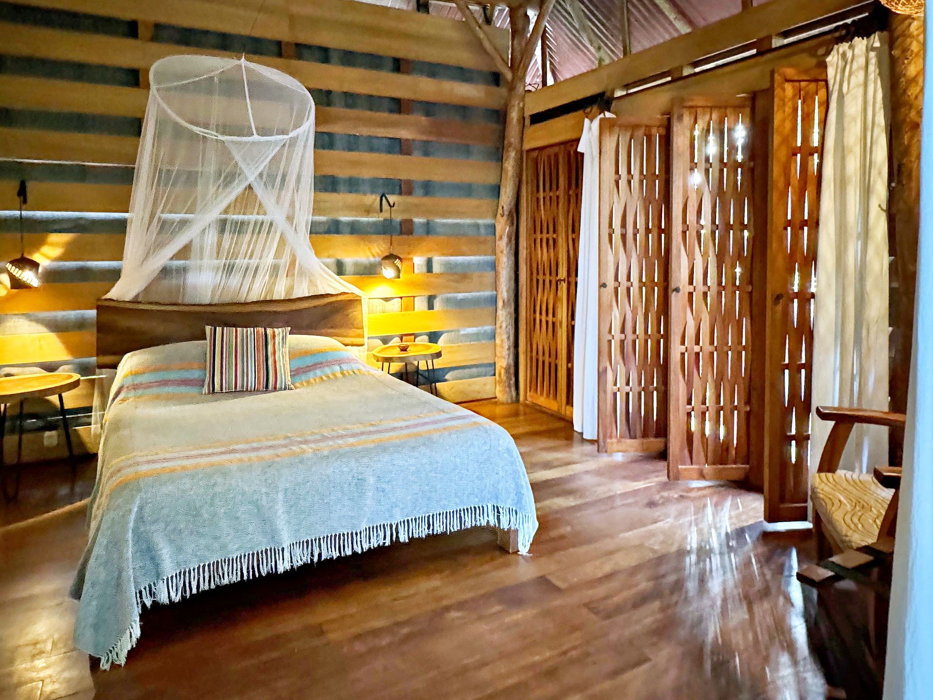 Bedroom with a bed, mosquito net, wooden doors, and hardwood floors.