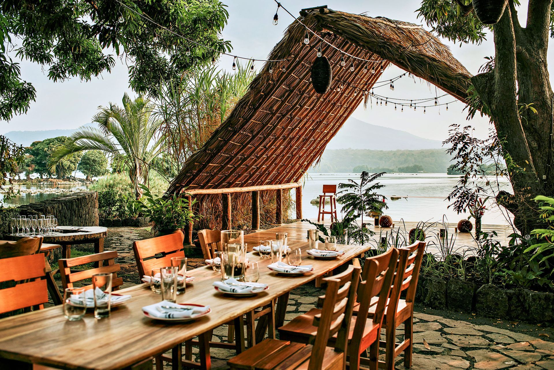 Outdoor dining table set for a meal, under a thatched roof, with ocean views.