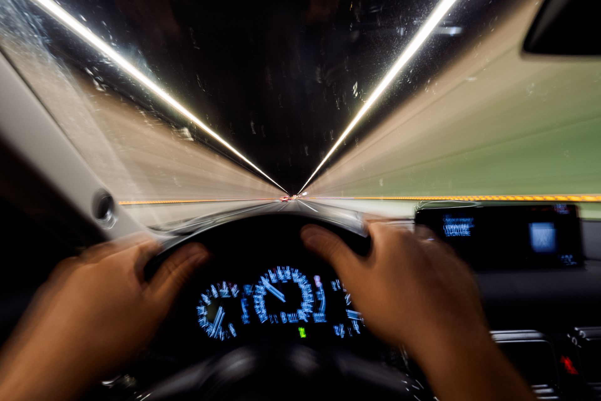 Driver’s view inside tunnel, dashboard, and hands on wheel in foreground. Driver’s view inside tunnel, dashboard, and hands on wheel in foreground.
