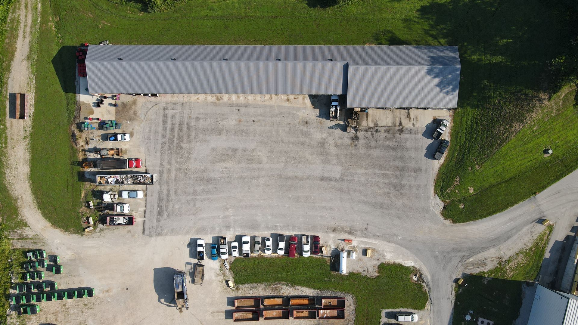 Aerial view of a large industrial building with a gravel lot. Various vehicles and equipment are present.