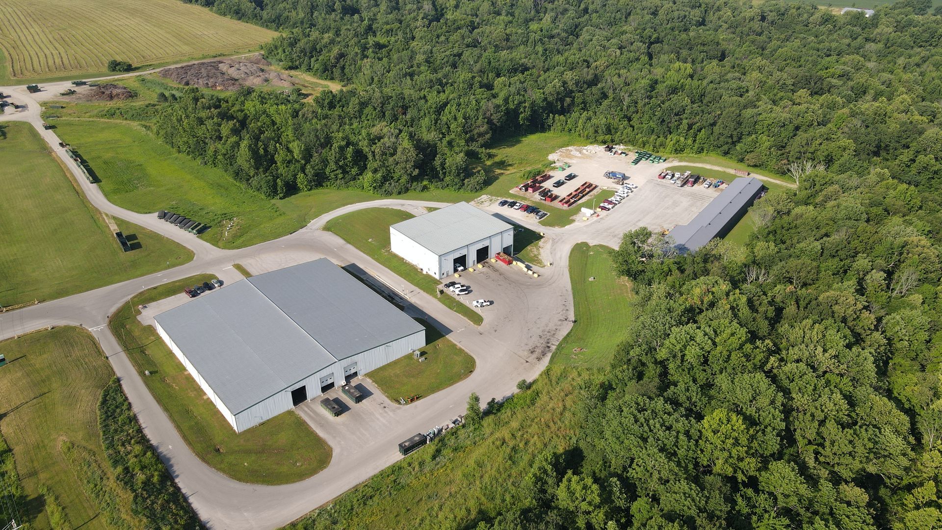 Aerial view of industrial buildings surrounded by greenery and a clearing.
