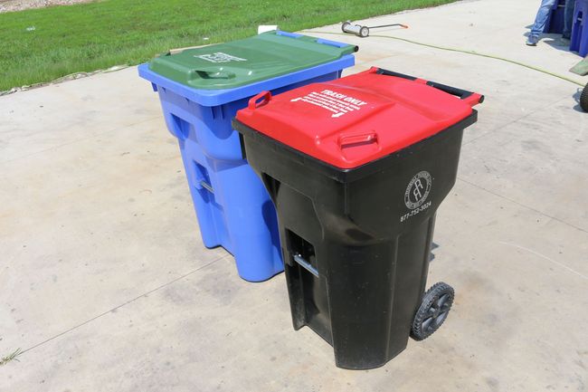 Two trash cans: one black with a red lid, the other blue with a green lid, sit on a concrete surface.