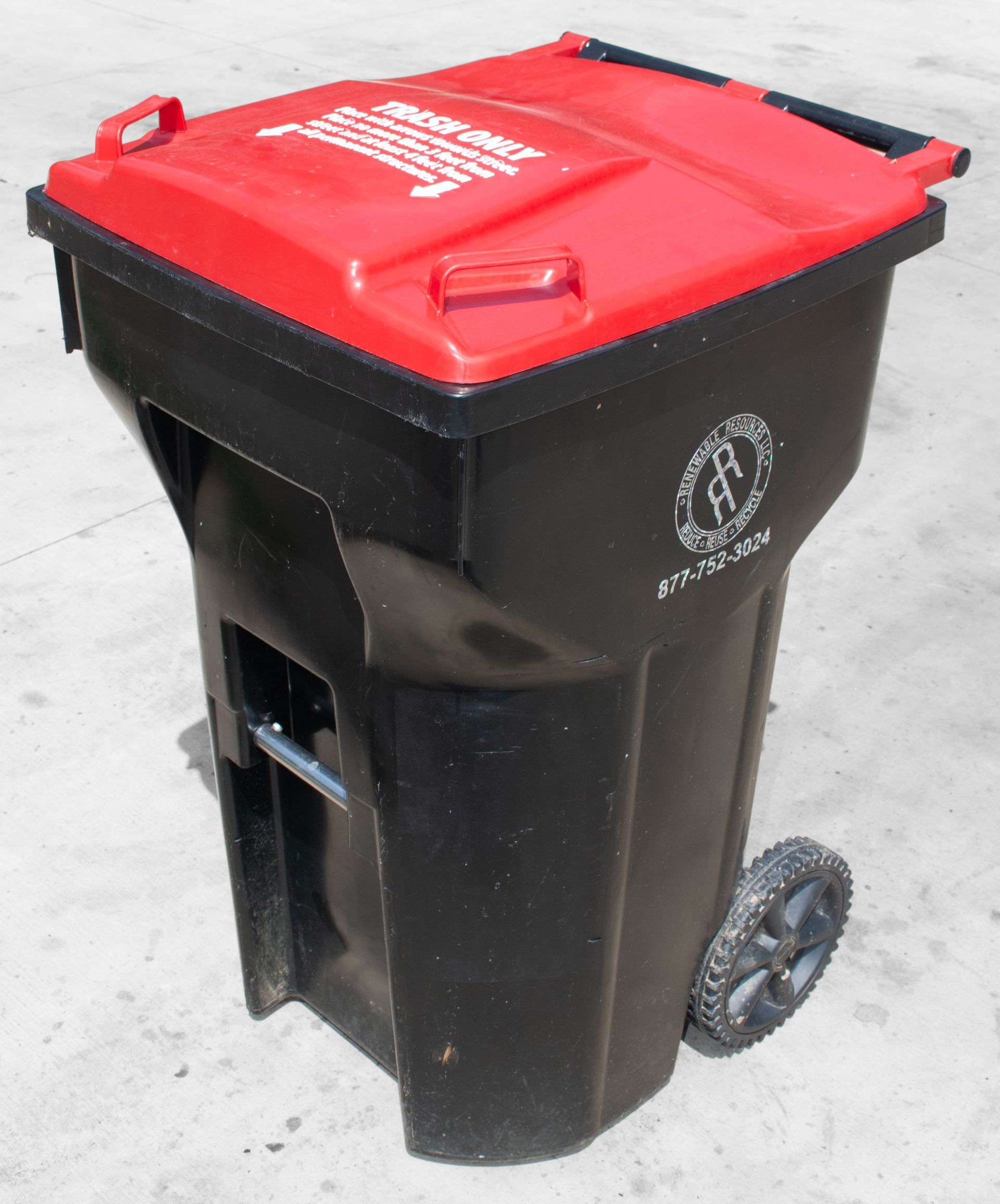 Black and red wheeled trash bin, with a logo, on a concrete surface.