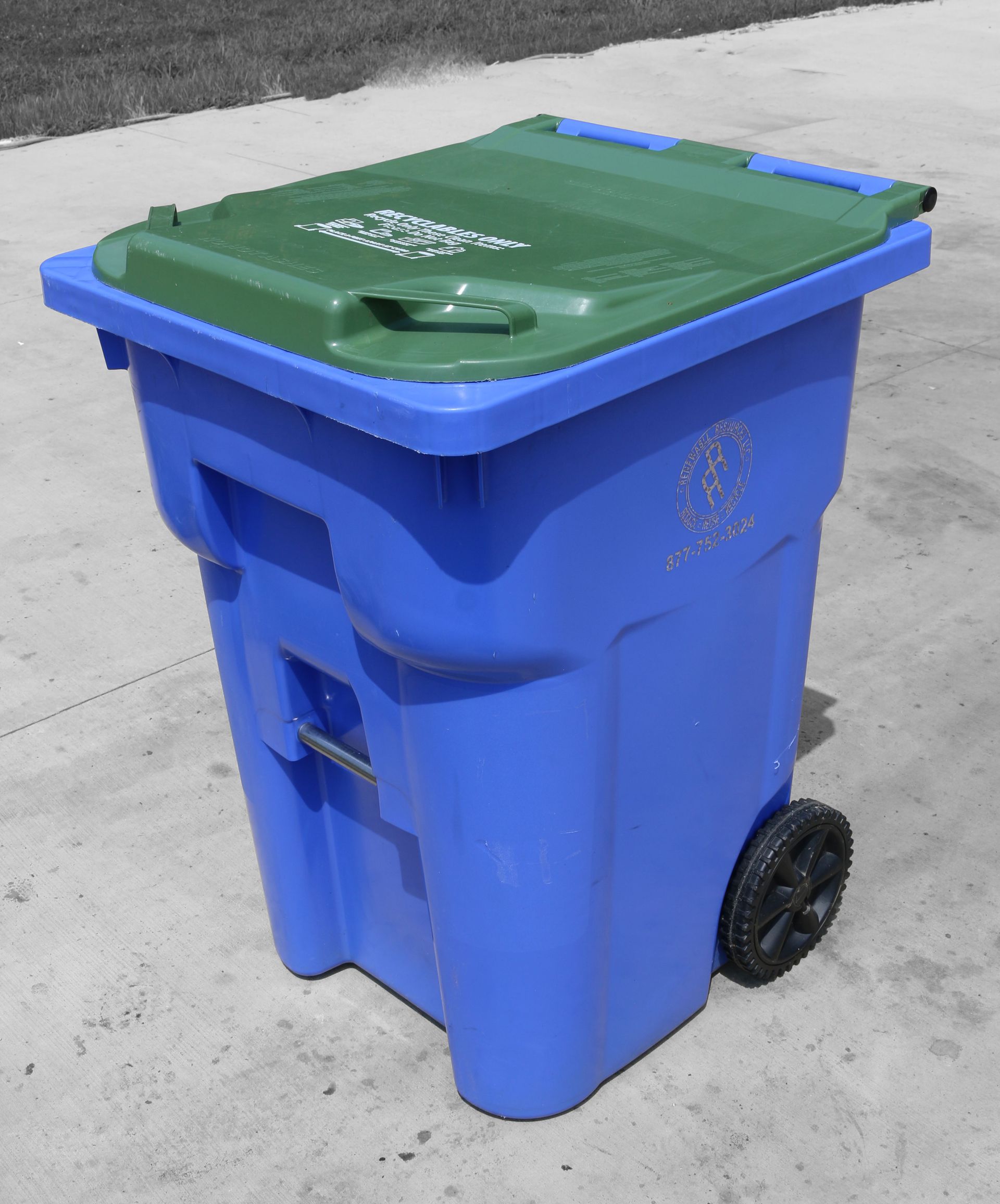 Blue recycling bin with a green lid and a black wheel, on a gray concrete surface.