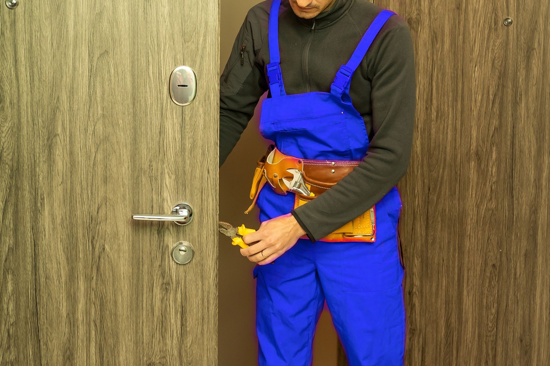 A man in blue overalls is working on a door