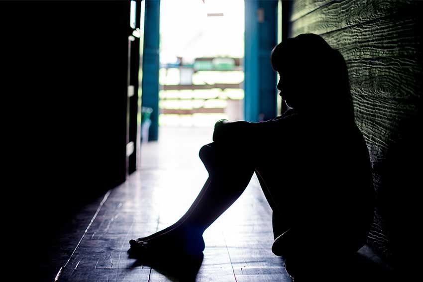 Silhouette of a person sitting alone in a dim hallway.
