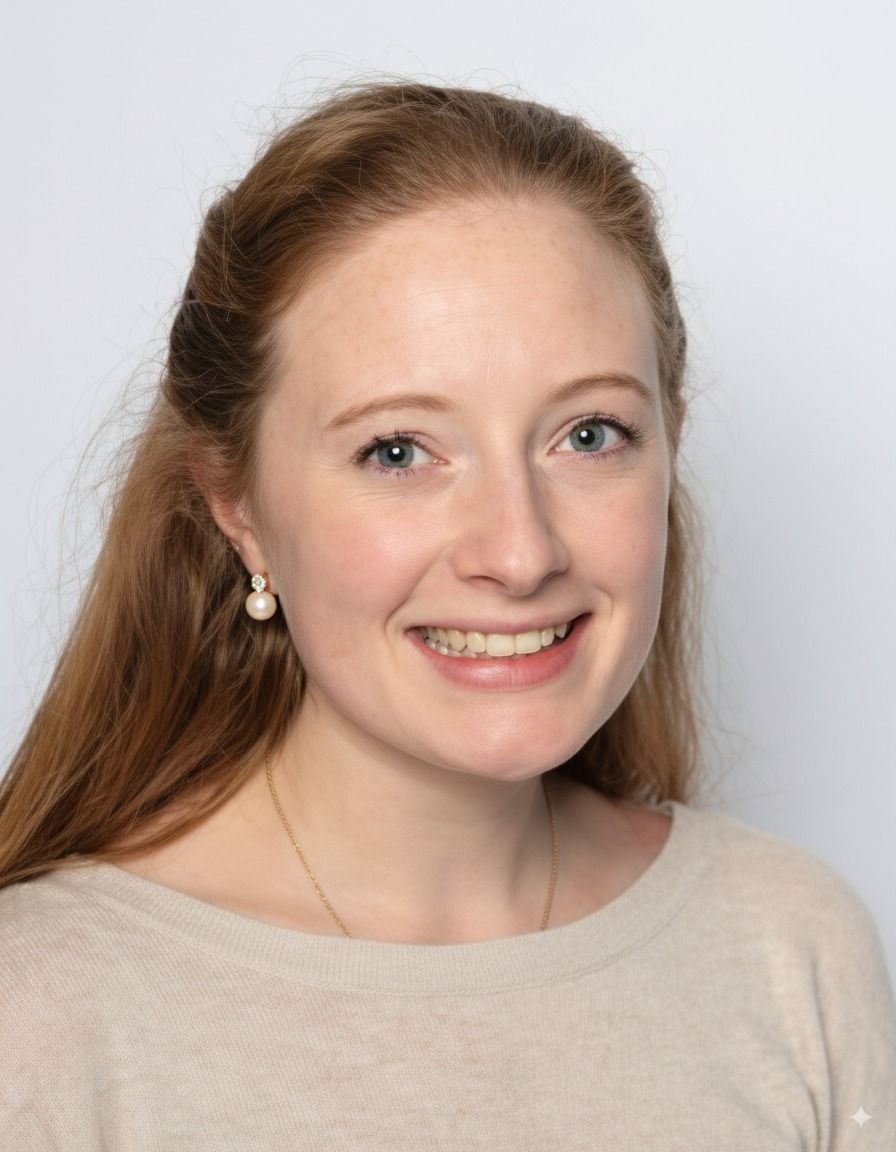 Woman with long reddish hair smiling, wearing a light-colored sweater and pearl earrings.