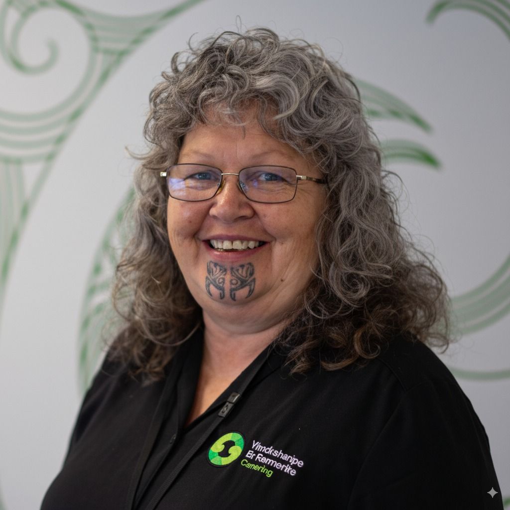 Woman with gray curly hair and glasses, smiling, wearing a black shirt, and a chin tattoo.