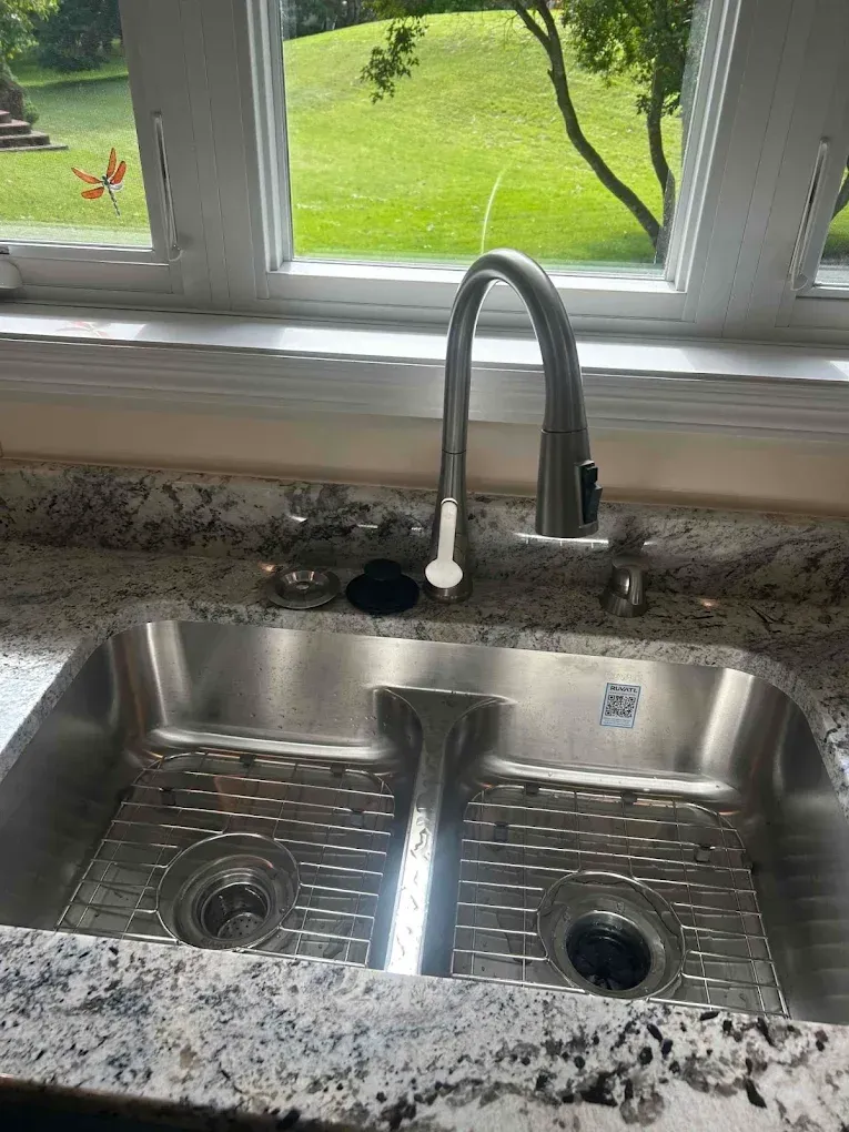 Stainless steel kitchen sink with faucet, granite countertop, and window overlooking a grassy yard.