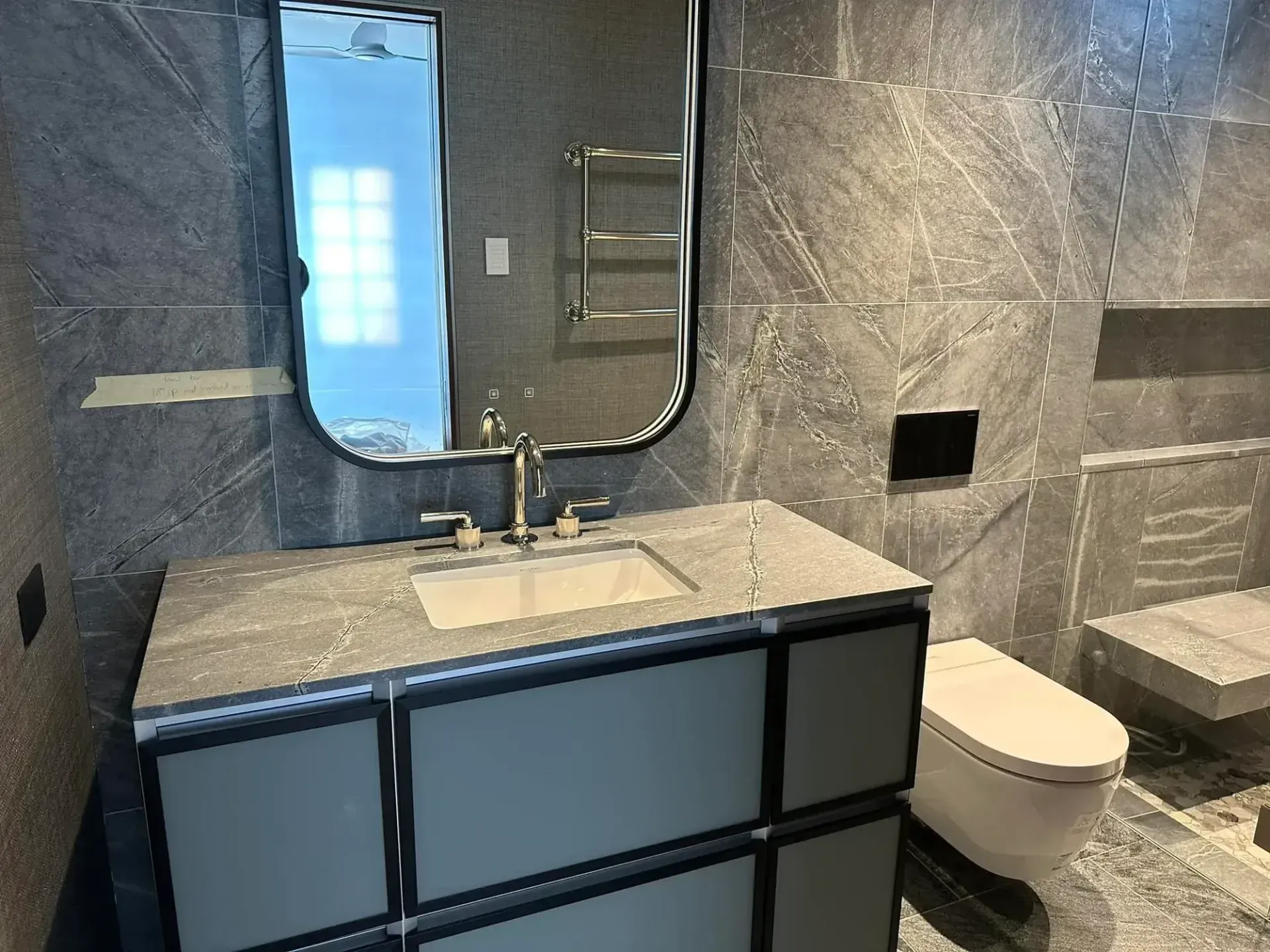 Modern bathroom with gray marble walls and vanity. Features a mirror, sink, and toilet.
