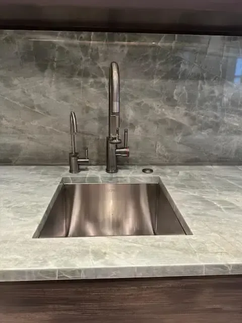 Stainless steel sink with two faucets and a button set into a pale green countertop.