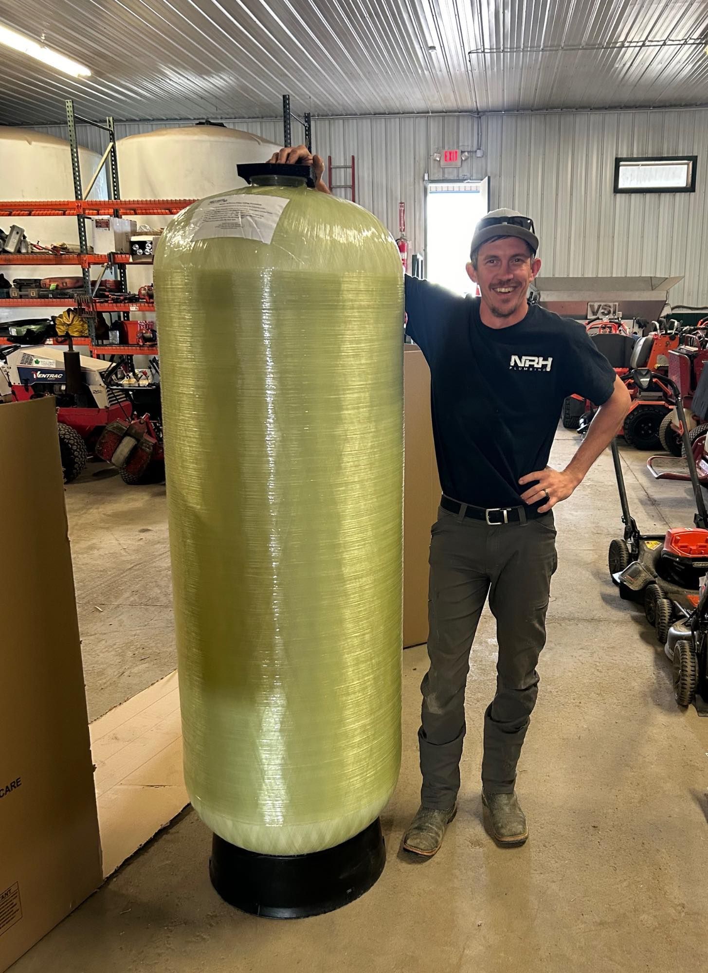 Man standing next to a large water filtration tank in a warehouse.