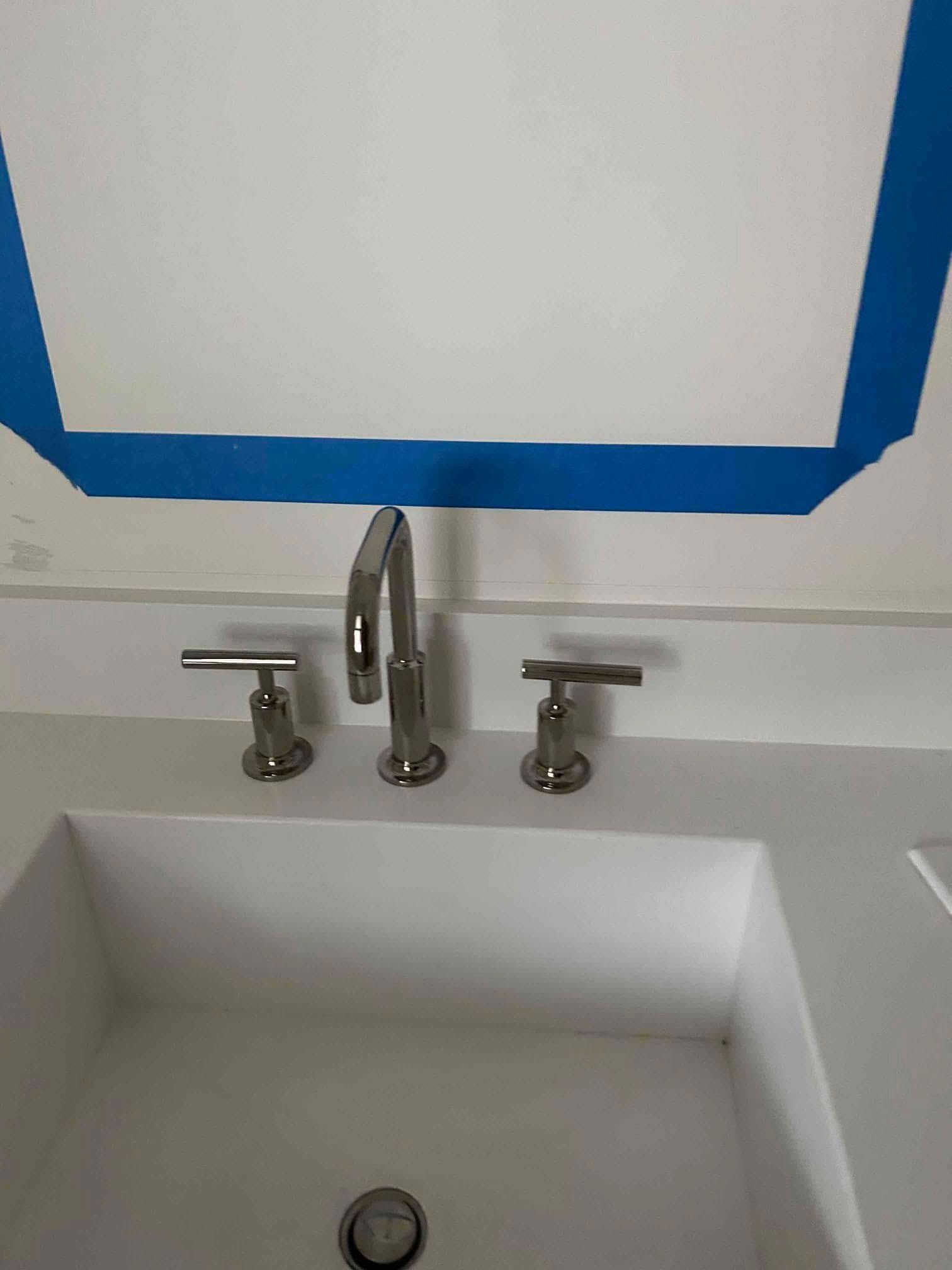 Bathroom sink with silver faucet and handles, blue tape along the top edge.