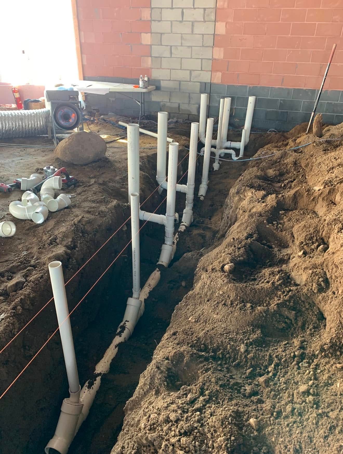 White PVC pipes in a trench, connected to a brick building.