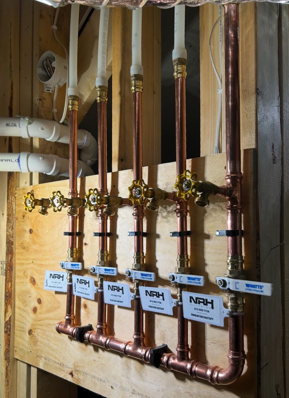Copper plumbing pipes and valves installed on plywood, with white supply lines.