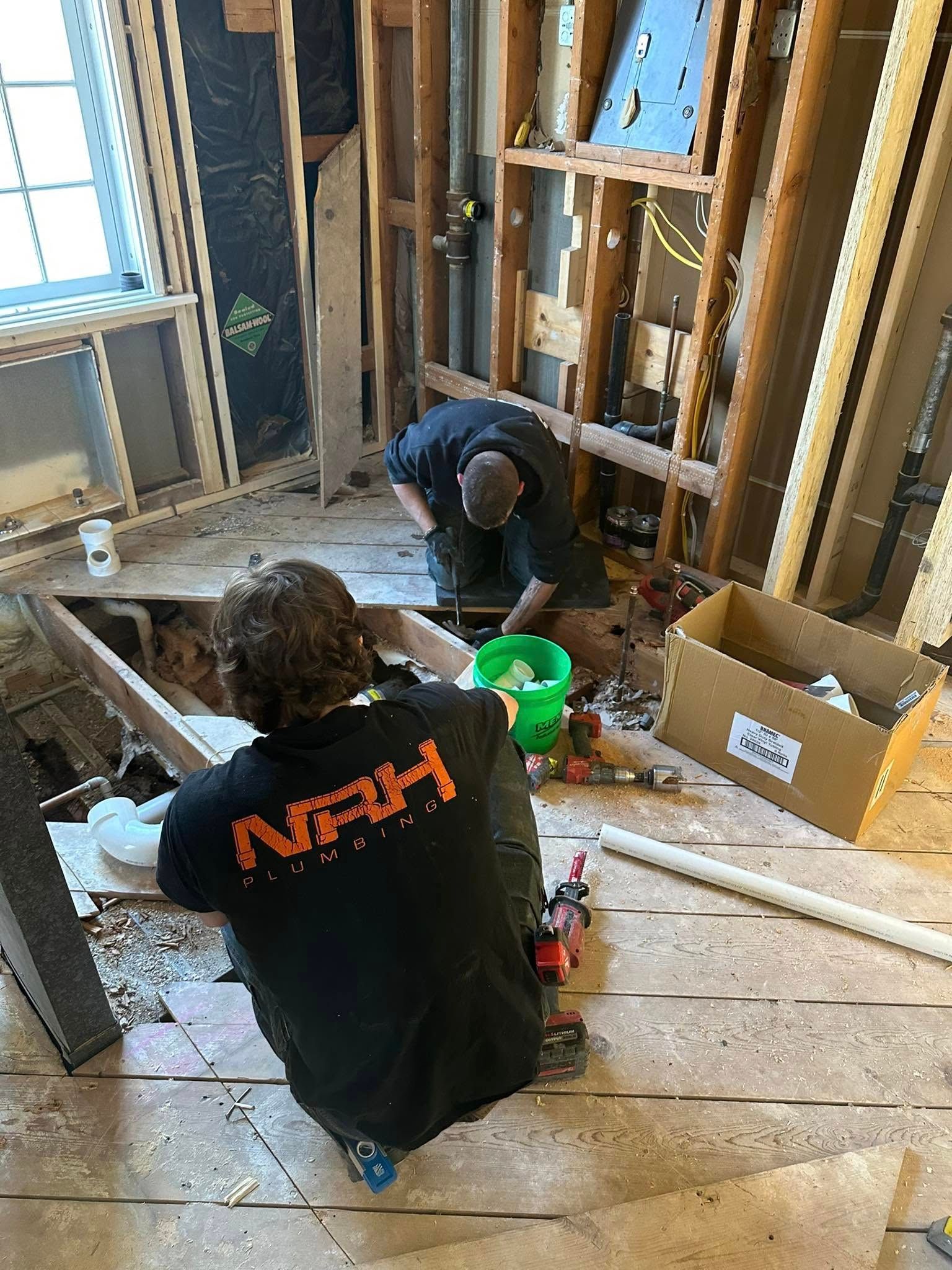 Two people working on construction in a room, surrounded by wooden framing and tools.