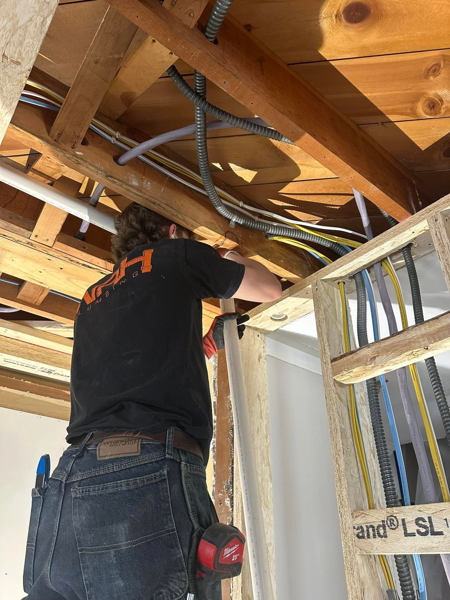 Electrician works on wiring in a ceiling, next to wooden studs.
