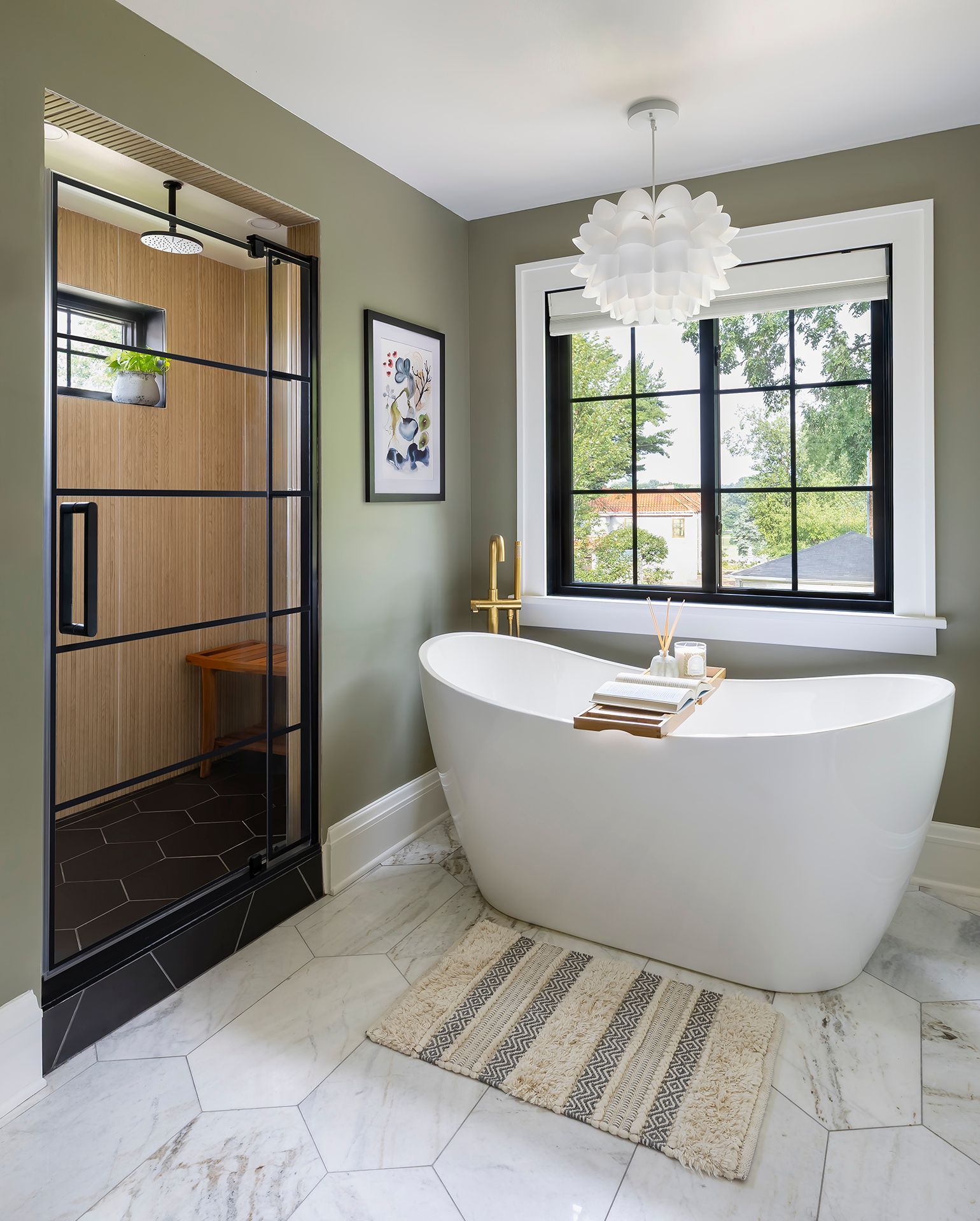 Freestanding white bathtub in a modern bathroom with marble walls and a black tiled accent.