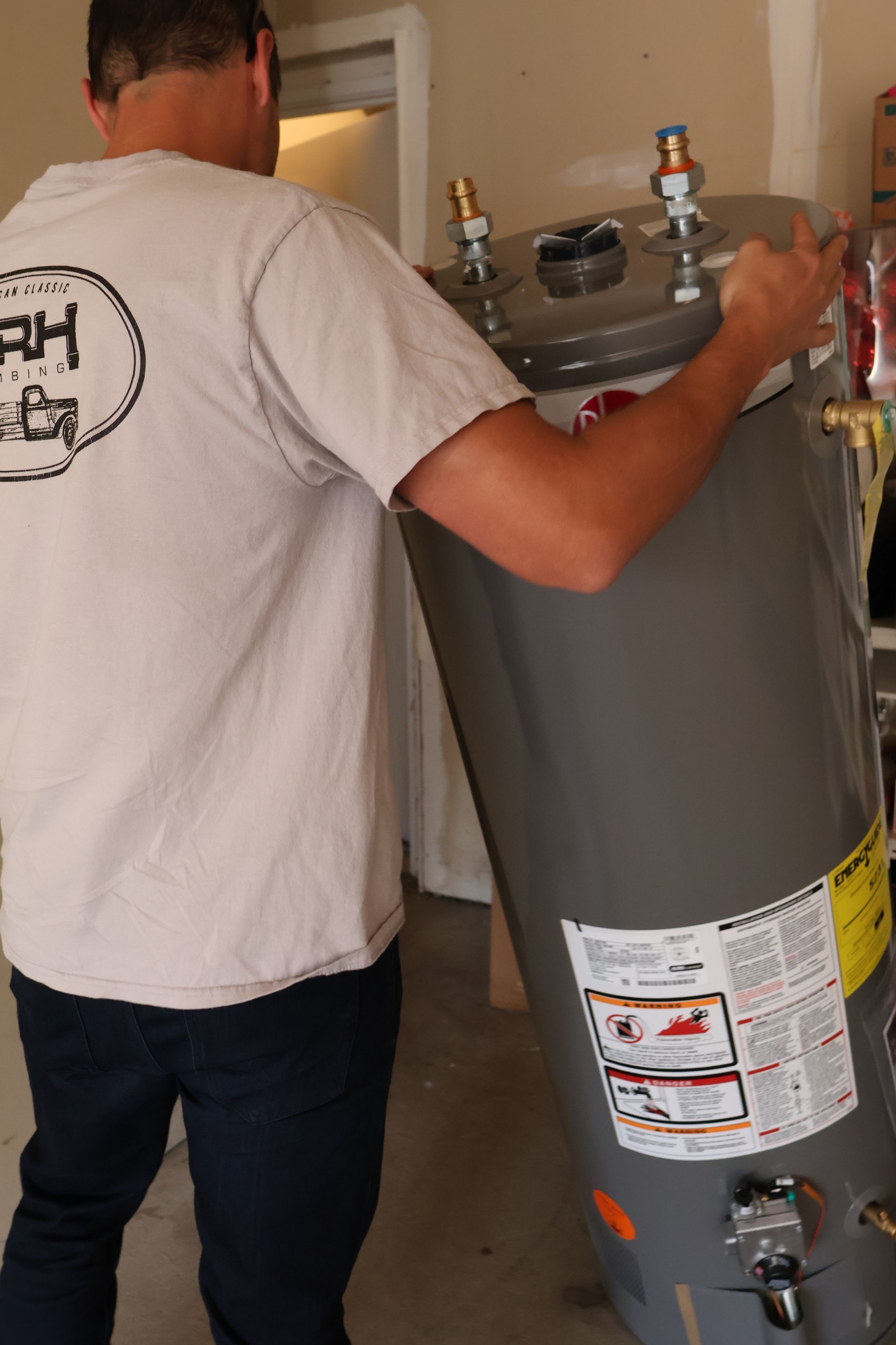 Person in black shirt and white hat working on a water heater in a closet.