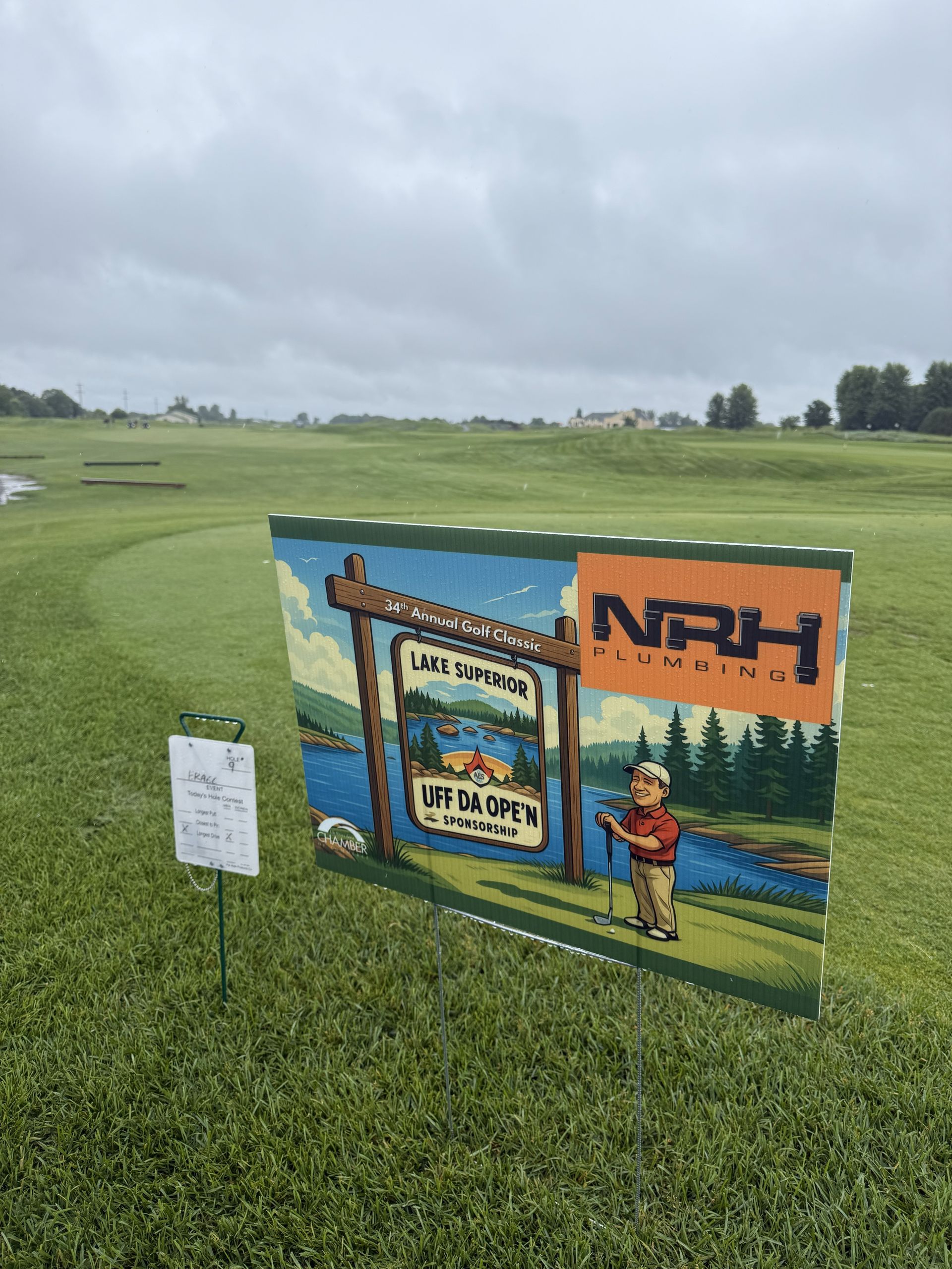 Sign for a golf tournament on a green course with a cloudy sky.