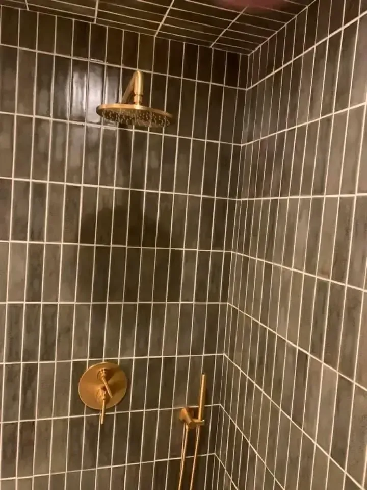 Gold shower fixtures against dark gray tiled walls.