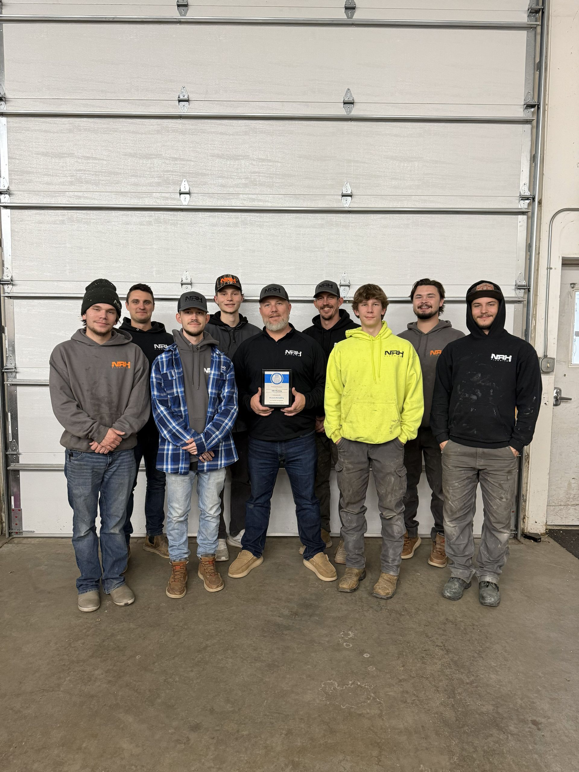 Group of men posing in front of a garage door, holding an award.