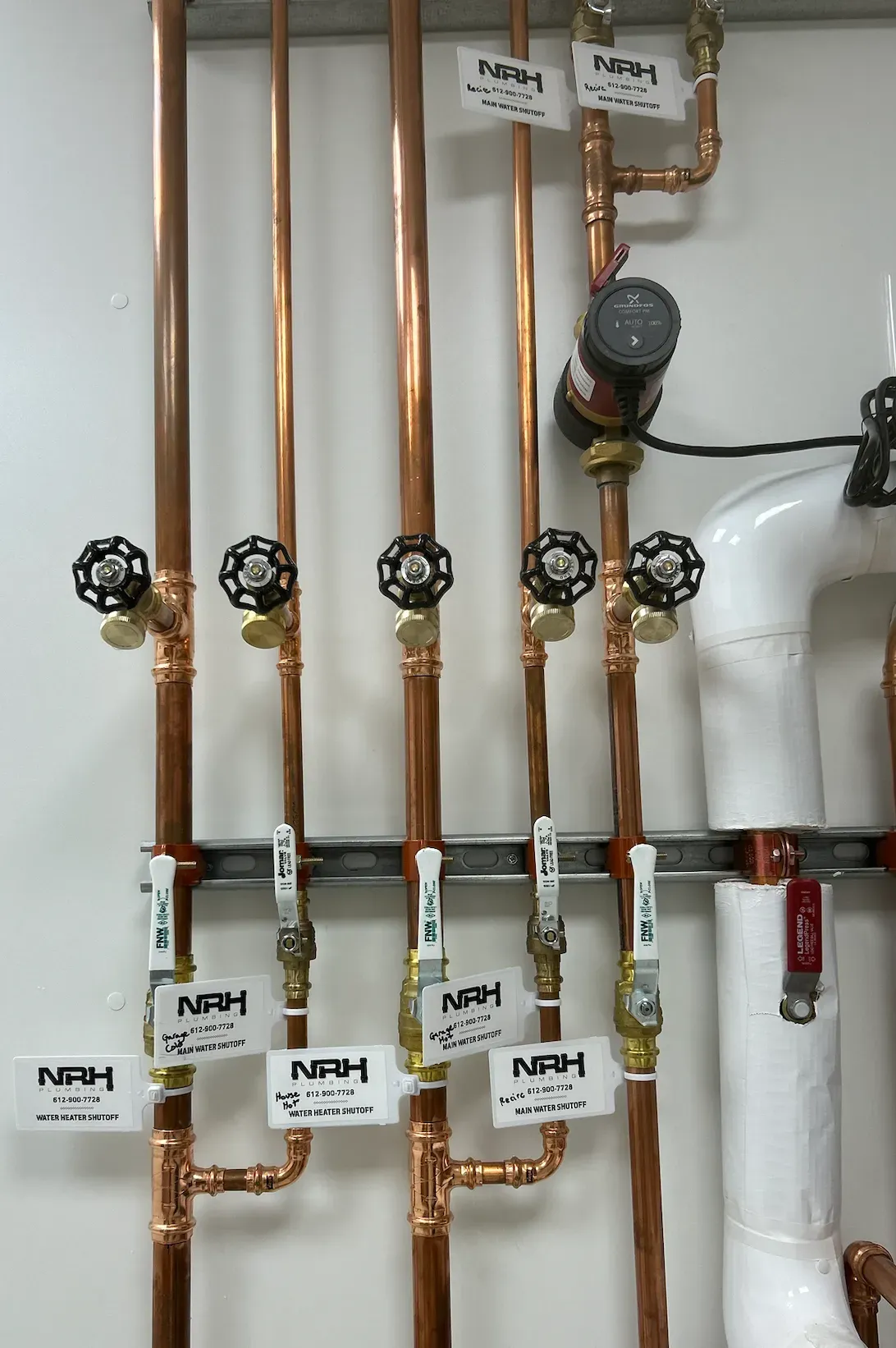 Copper pipes with valves and labels mounted on a white wall.