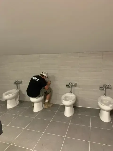 A person sitting on a toilet in a row of bathroom stalls.