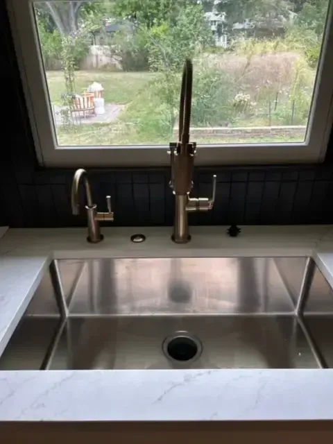 Stainless steel kitchen sink with faucet and window view of outdoor landscape.