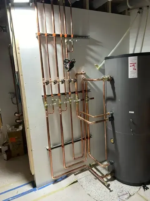 Copper pipes arranged on a white wall, connecting to a black water heater.