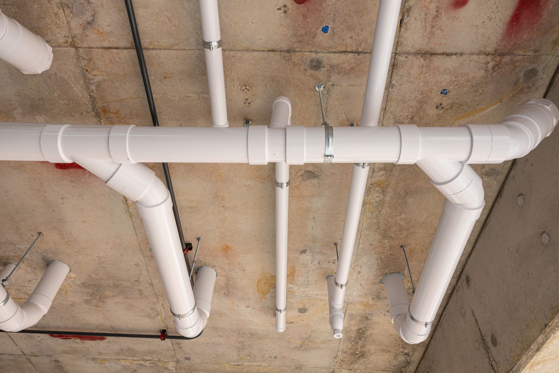 White PVC pipes attached to a concrete ceiling in a construction setting.