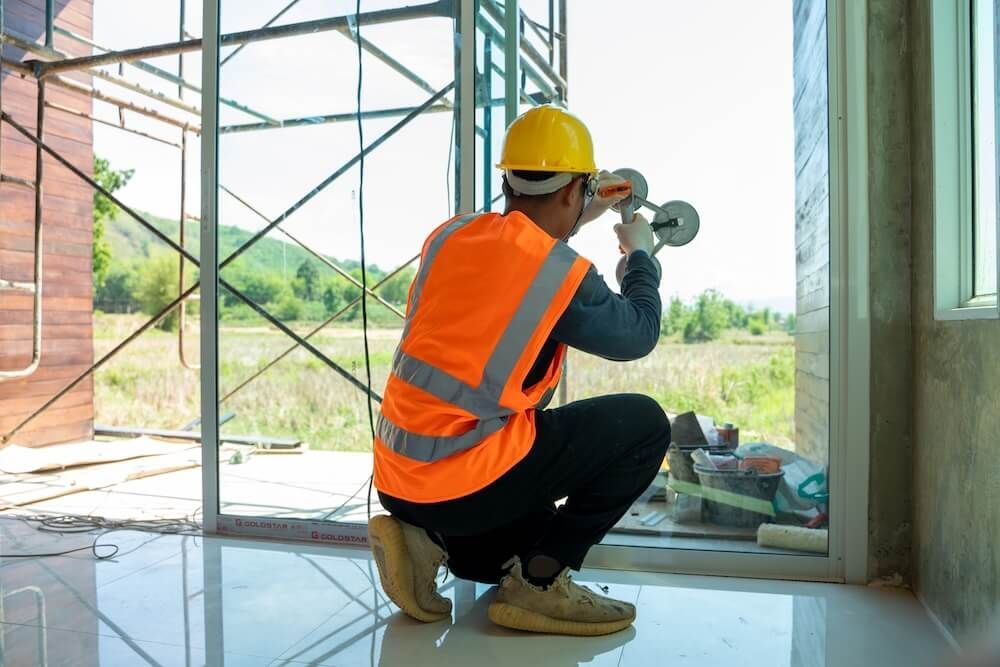 A construction worker is installing a window in a building under construction — Reflect Glass In Tuggerah, NSW
