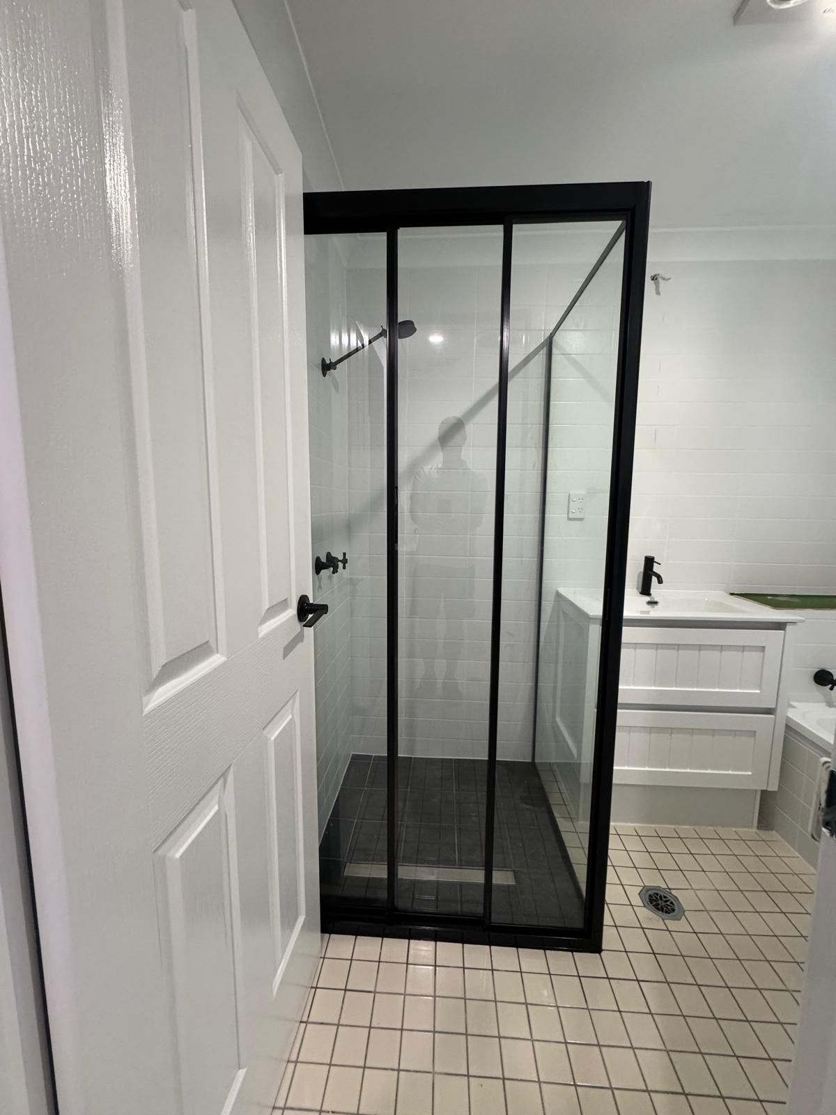 A Bathroom with A Sliding Glass Shower Door and A Black Frame — Reflect Glass In Tuggerah, NSW