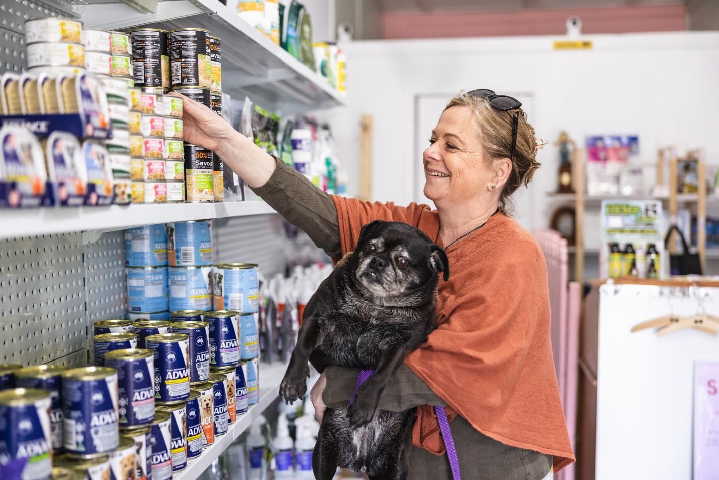 A Woman is Holding a Black Dog in Her Arms While Shopping for Dog Food — Fluffy Paws Pet Grooming In Wingham, NSW