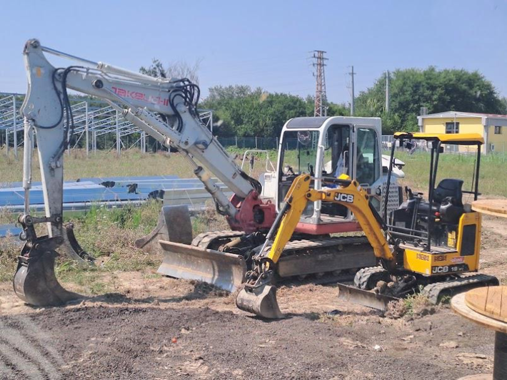Un grande escavatore bianco e un escavatore JCB più piccolo di colore giallo parcheggiati fianco a fianco in un cantiere sterrato.