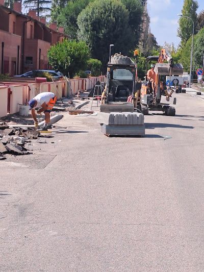 Operai edili manovrano macchinari pesanti su una strada soleggiata vicino a un complesso residenziale.