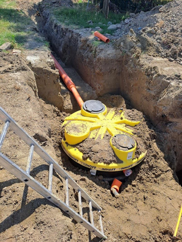 Una fossa settica o serbatoio di servizio interrato, di forma circolare e di colore giallo, è installata in una trincea a cielo aperto e collegata a tubi in PVC arancioni.