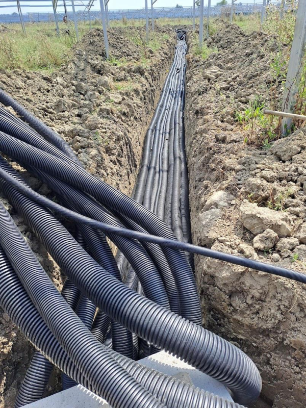 Una profonda e stretta trincea in un campo erboso contiene numerosi tubi corrugati di plastica nera disposti in fila.