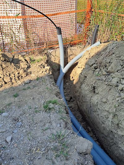 Una trincea nel terreno contenente diversi tubi per impianti elettrici di colore blu e bianco che emergono dalla terra.