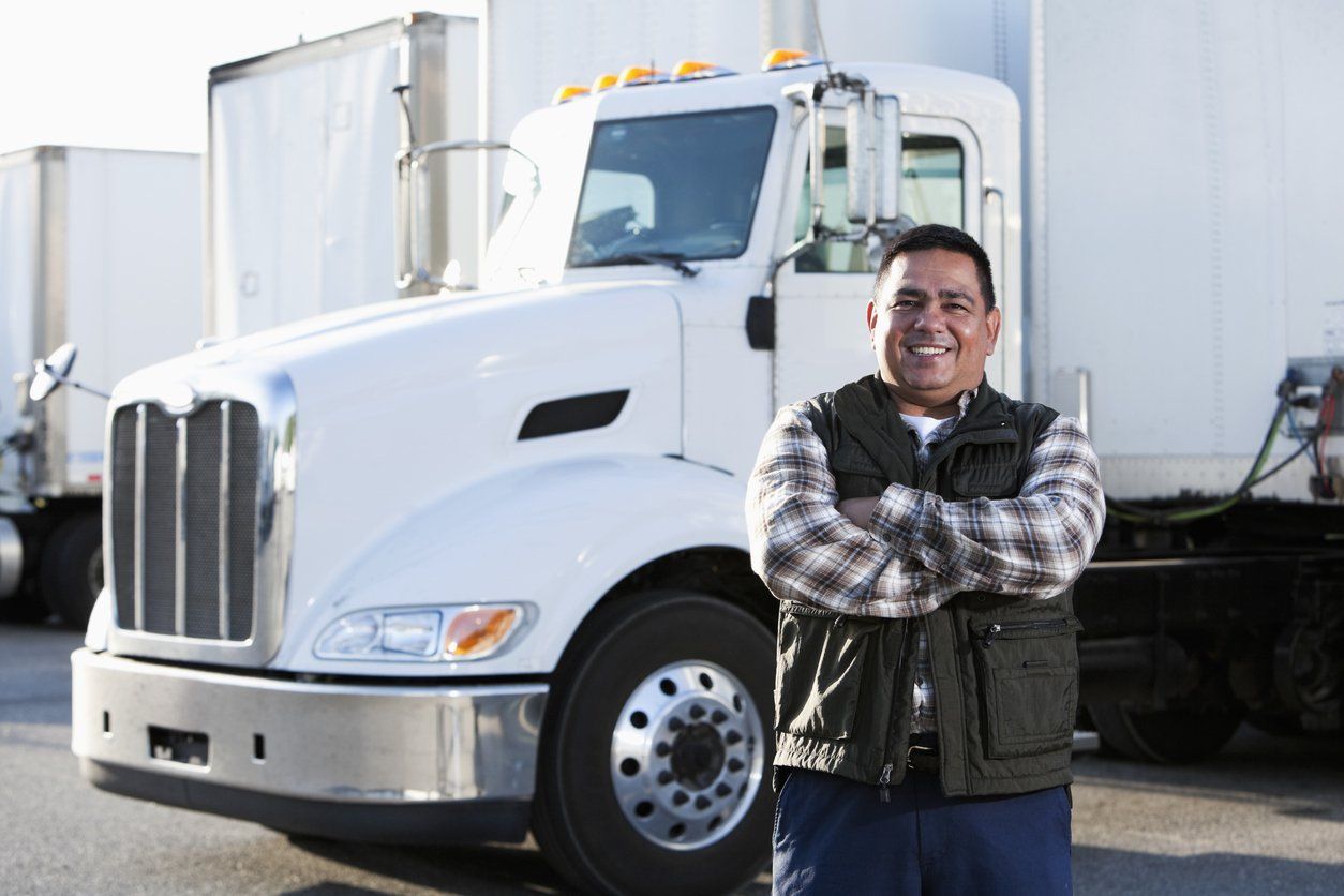 Portrait of a male truck driver standing in a parking lot dedicated to big trucks with his white truck in the background.
