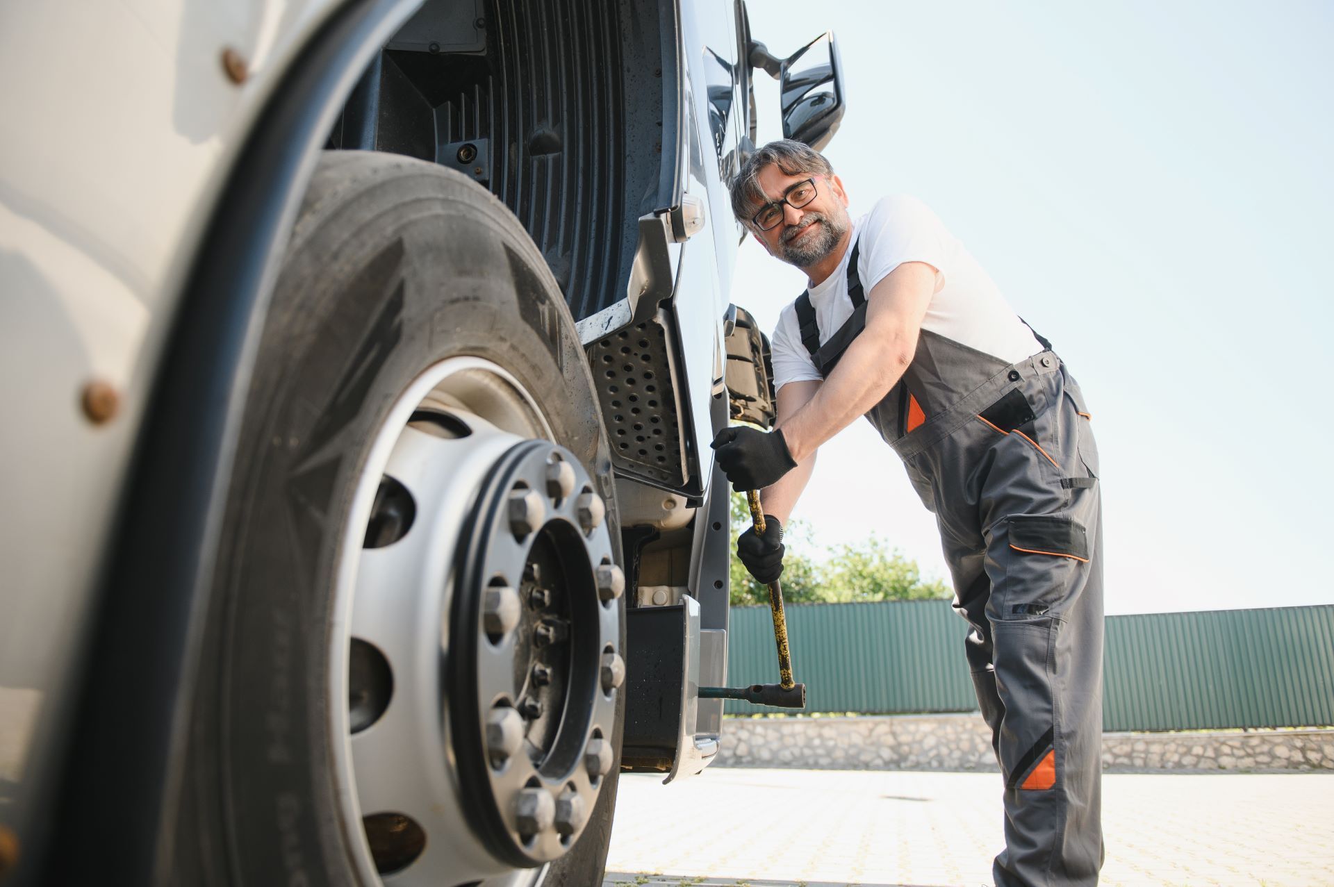 Mechanic in gray overalls working on a semi-truck tire, outdoors.