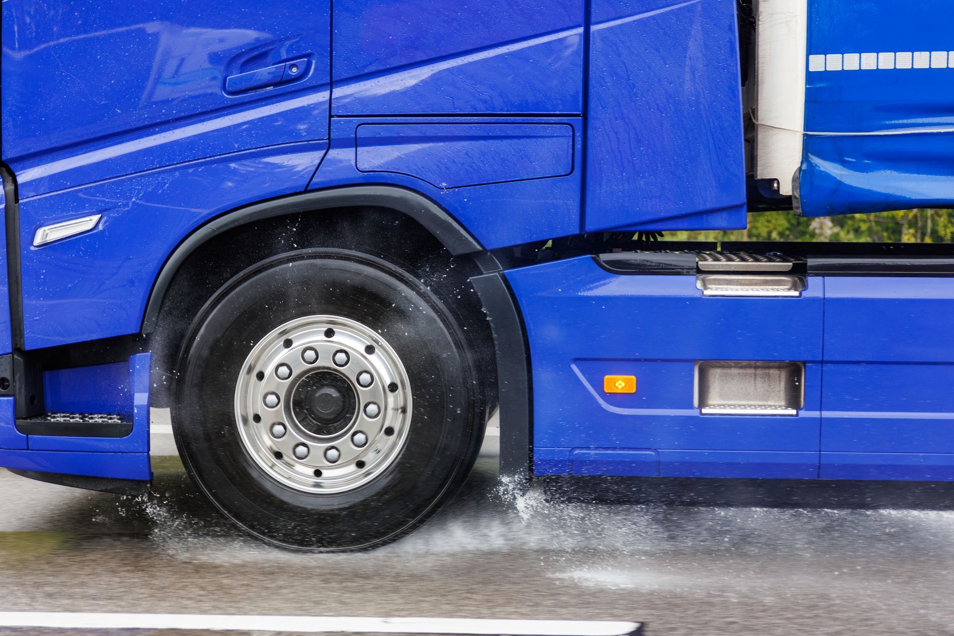 A blue semi truck is driving through a puddle of water.