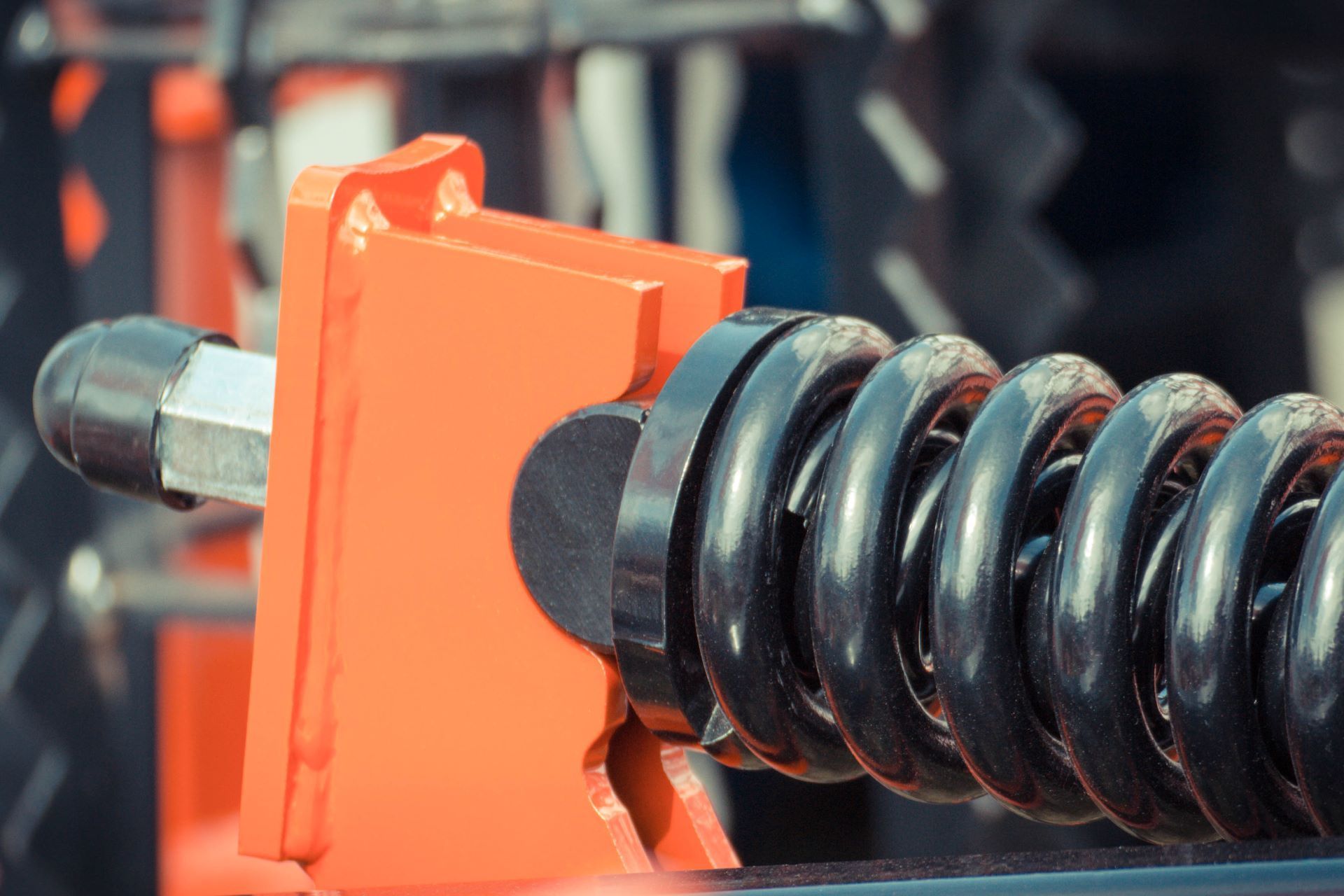 Orange metal bracket with a black coil spring and bolt.