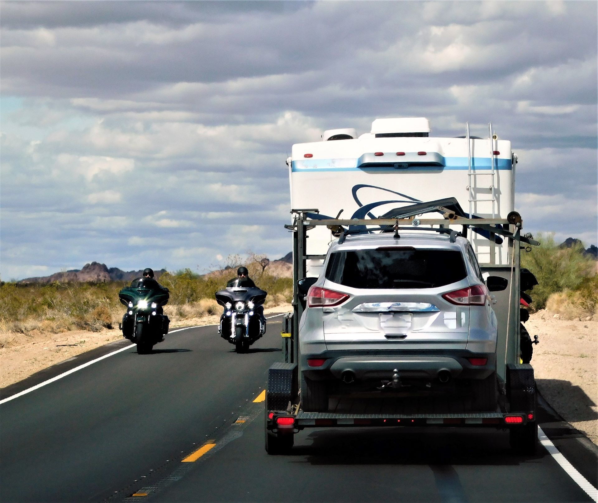 A car is being towed by a trailer with a rv on top of it