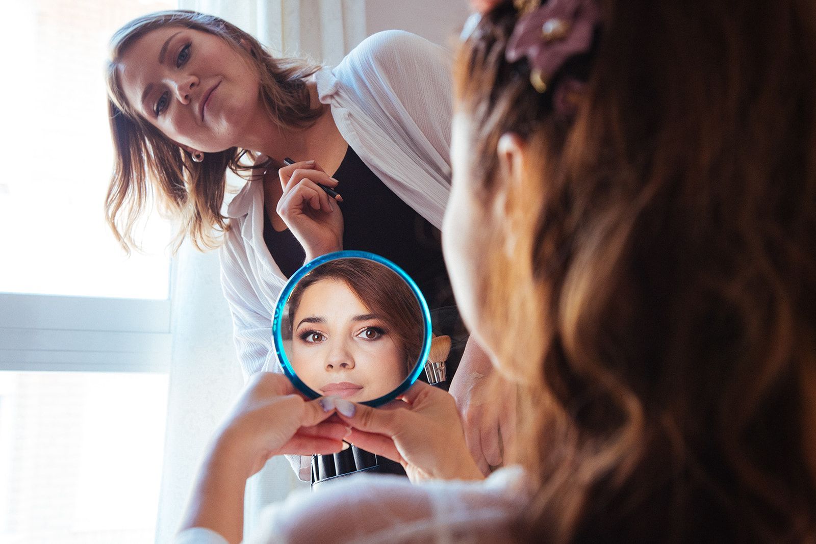 Novia mirándose al espejo durante su sesión de maquillaje el día de su boda en Valencia, España.