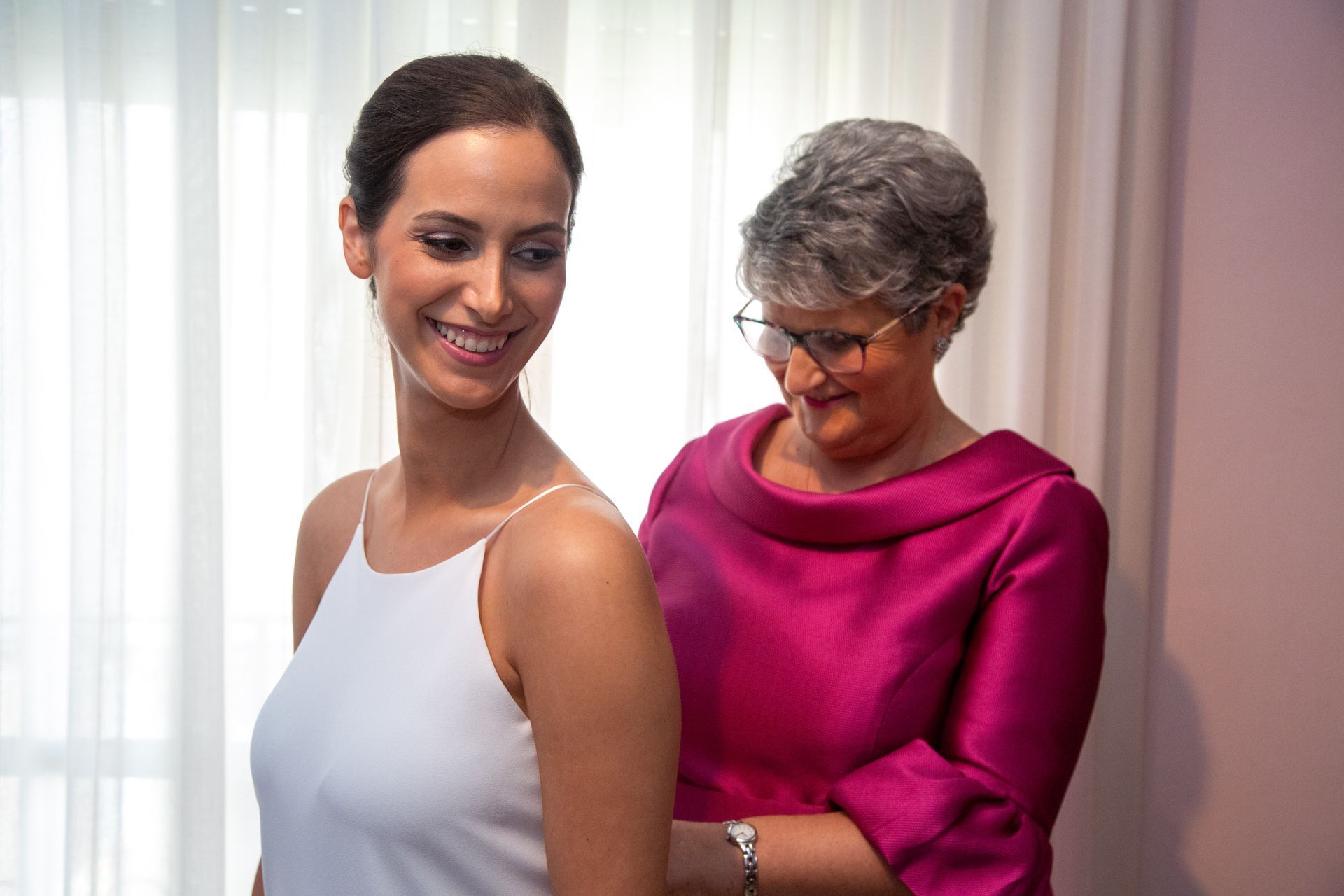 Madre de la novia ayudando a su hoja a abrochar su vestido el día de la boda.