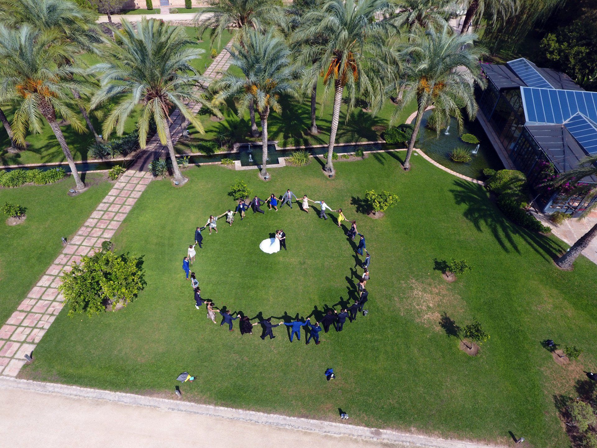 Vista aérea con dron de los novios y sus amigos formando un círculo en el Huerto de Santa María del Puig en Valencia, en un momento de complicidad y amistad en su celebración nupcial. Fotógrafo Valencia