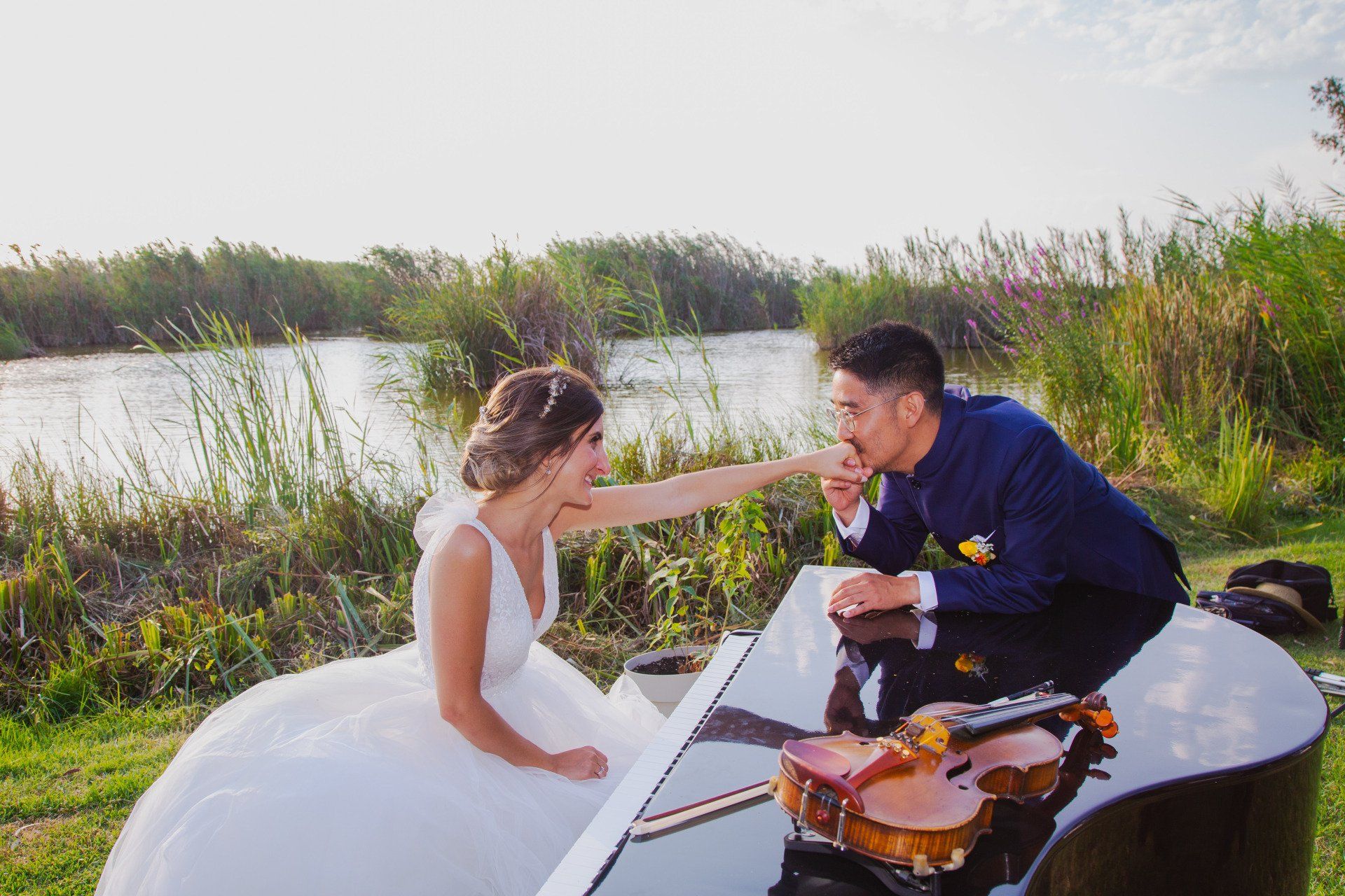 Fotógrafo de bodas capturando una imagen romántica de un novio apoyado en un piano besando gentilmente la mano a su novia en el elegante entorno del Restaurante Nou Racó de Valencia, en un momento lleno de amor y ternura.
