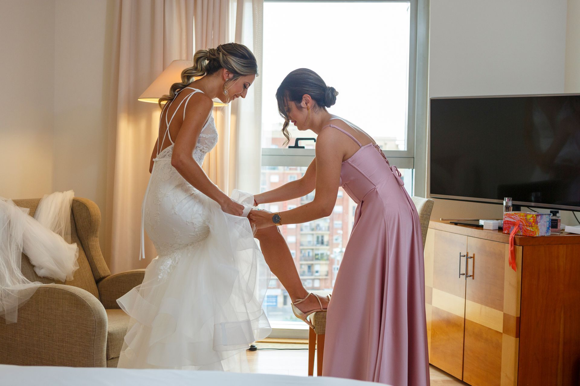 Hermana ayudando a la novia a ponerse la liga el día de su boda en Valencia. 