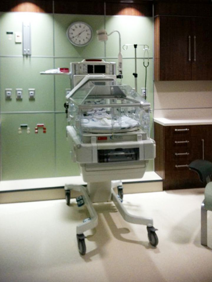A hospital room with a clock on the wall and a baby incubator